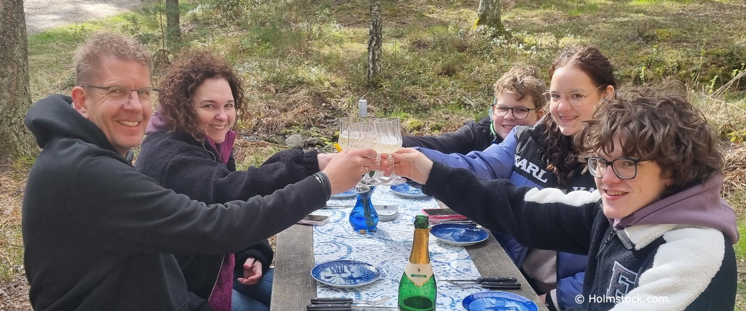 Gezinsreis naar Stockholm, Zweden. Holmstock Travel. Gezellige gezinsfoto bij het outdoor dinner dat op het open vuur bereid wordt. Skärgården bij prachtig mooi weer in April 2026